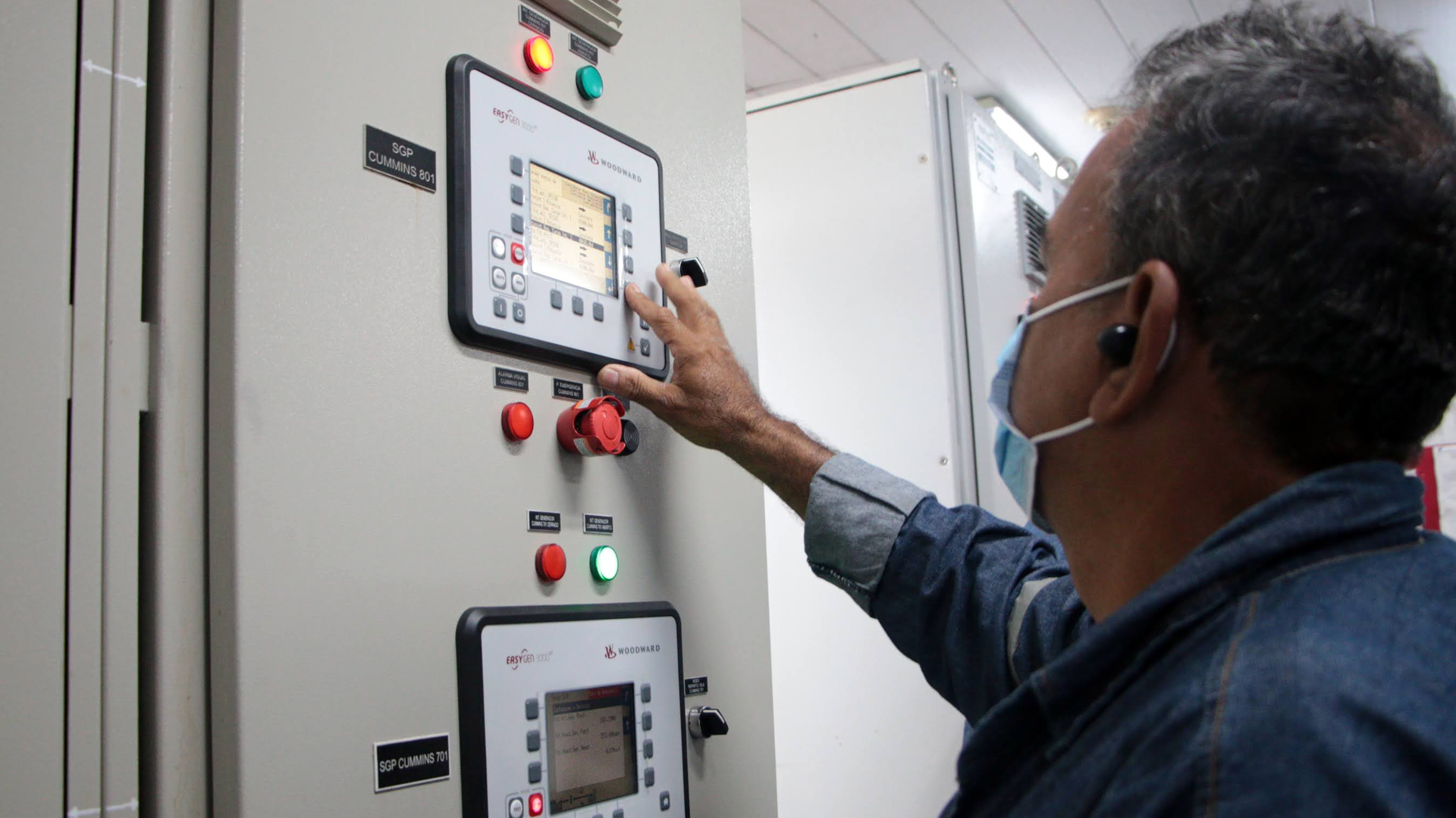 Un hombre con camisa azul está tocando un panel de control, de una central de energía 