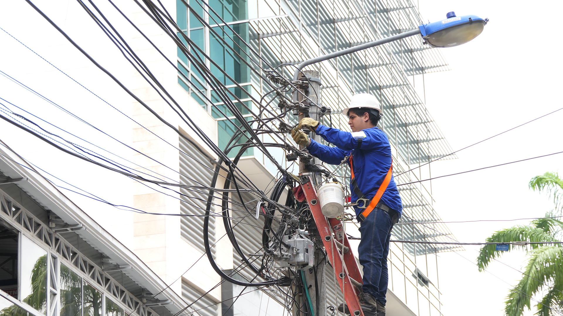 Un trabajador en un poste de energía eléctrica, utilizando herramientas y equipado con medidas de seguridad adecuadas.